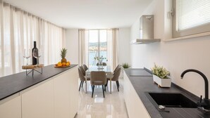 A modern kitchen with a dining area, large windows, and a view of the sea.