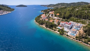 An aerial view of a coastal town with buildings along the shoreline, clear blue waters, and a small island in the distance.