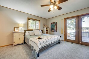 A bedroom with a bed, a nightstand, a ceiling fan, a window, and a door leading to a balcony. - Delton Oasis Retreat w/ Lake Views & Deck! (Delton)