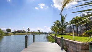 A wooden dock leading to calm water, surrounded by greenery and a clear sky. - South Gulf Cove 3 Bedroom Canal Pool Home (Port Charlotte)