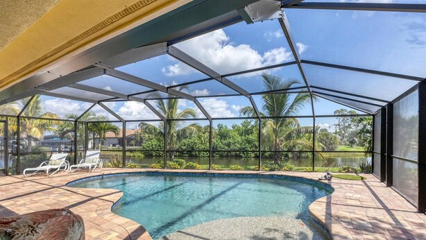 A covered outdoor swimming pool with a view of a lake and palm trees. - South Gulf Cove 3 Bedroom Canal Pool Home (Port Charlotte)