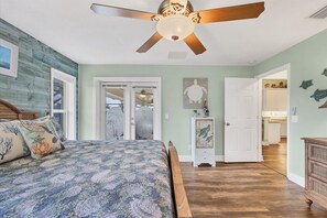 Un dormitorio con cama, ventilador de techo y puerta que da a otra habitación.