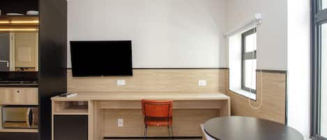 A hotel room with a bed, a desk, a TV mounted on the wall, a chair, and a small table.