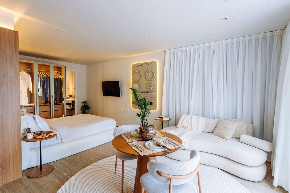 Une chambre d’hôtel comprenant un lit, un canapé, une table à manger agrémentée d’un vase de fleurs, une télévision et un miroir.