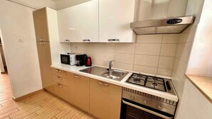 Una cocina compacta con gabinetes blancos, un lavamanos de acero inoxidable, una estufa a gas y un horno empotrado.