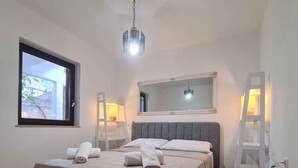 Un dormitorio con una cama, una ventana, un espejo, una escalera y una lámpara colgante.