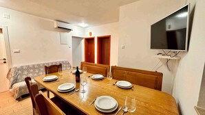 Un comedor con una mesa de madera dispuesta para seis personas, un televisor montado en la pared y una puerta que da a otra habitación.