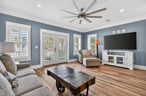 Un salon comprenant un ventilateur de plafond, un canapé, une table basse, un meuble pour la télévision et un buffet.