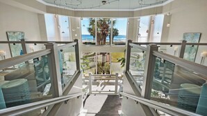 Ein modernes Hotelinterior mit einer Glasstiege, die zu einem Balkon mit Meerblick führt.