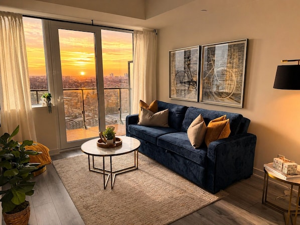 A living room with a blue sofa, a coffee table, and a city view through a large window.