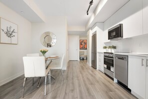 Une cuisine moderne avec des meubles blancs, des appareils en acier inoxydable et un coin repas comprenant des chaises et une table, le tout dans des tons blancs.