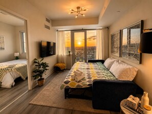 A modern bedroom with a large bed, a sofa, a TV, and a city view.