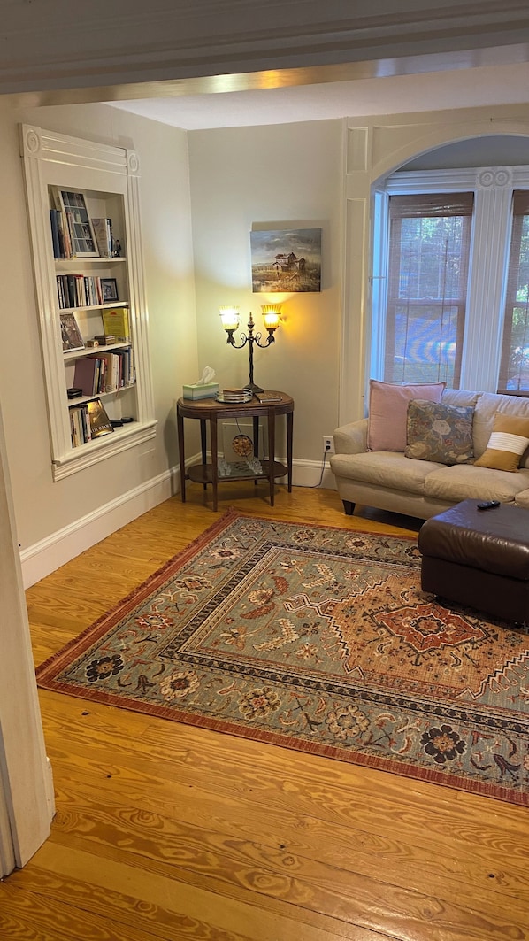 A living room with a bookshelf, a table with a lamp, a sofa, and a large rug.