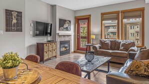 A living room with a fireplace, a sofa, a TV, and a dining area with a table and chairs. - Heated Pool, Hot Tubs, and Comfort for 6: Your Desired Canmore Escape! (Canmore)