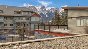 A multi-story building with balconies, a stone facade, and a view of snow-capped mountains. - Heated Pool, Hot Tubs, and Comfort for 6: Your Desired Canmore Escape! (Canmore)