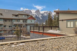 A multi-story building with balconies, a stone facade, and a view of snow-capped mountains. - Heated Pool, Hot Tubs, and Comfort for 6: Your Desired Canmore Escape! (Canmore)