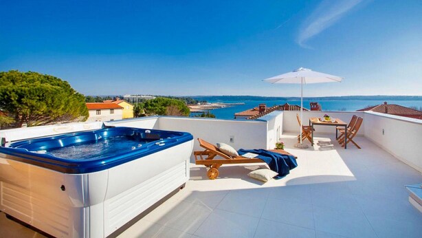 En takterrass med ett bubbelbad, utomhusmöbler och utsikt över havet.
