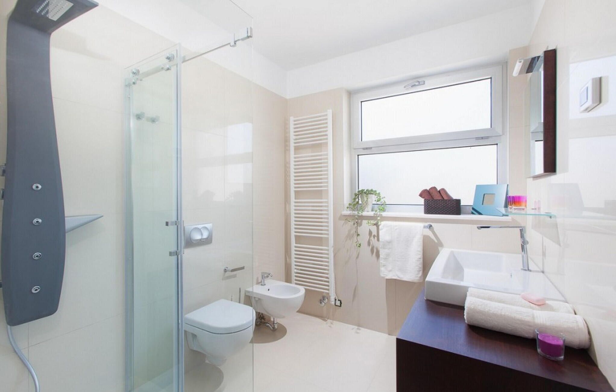 A modern bathroom with a glass shower enclosure, a toilet, a sink, and a window with a view.