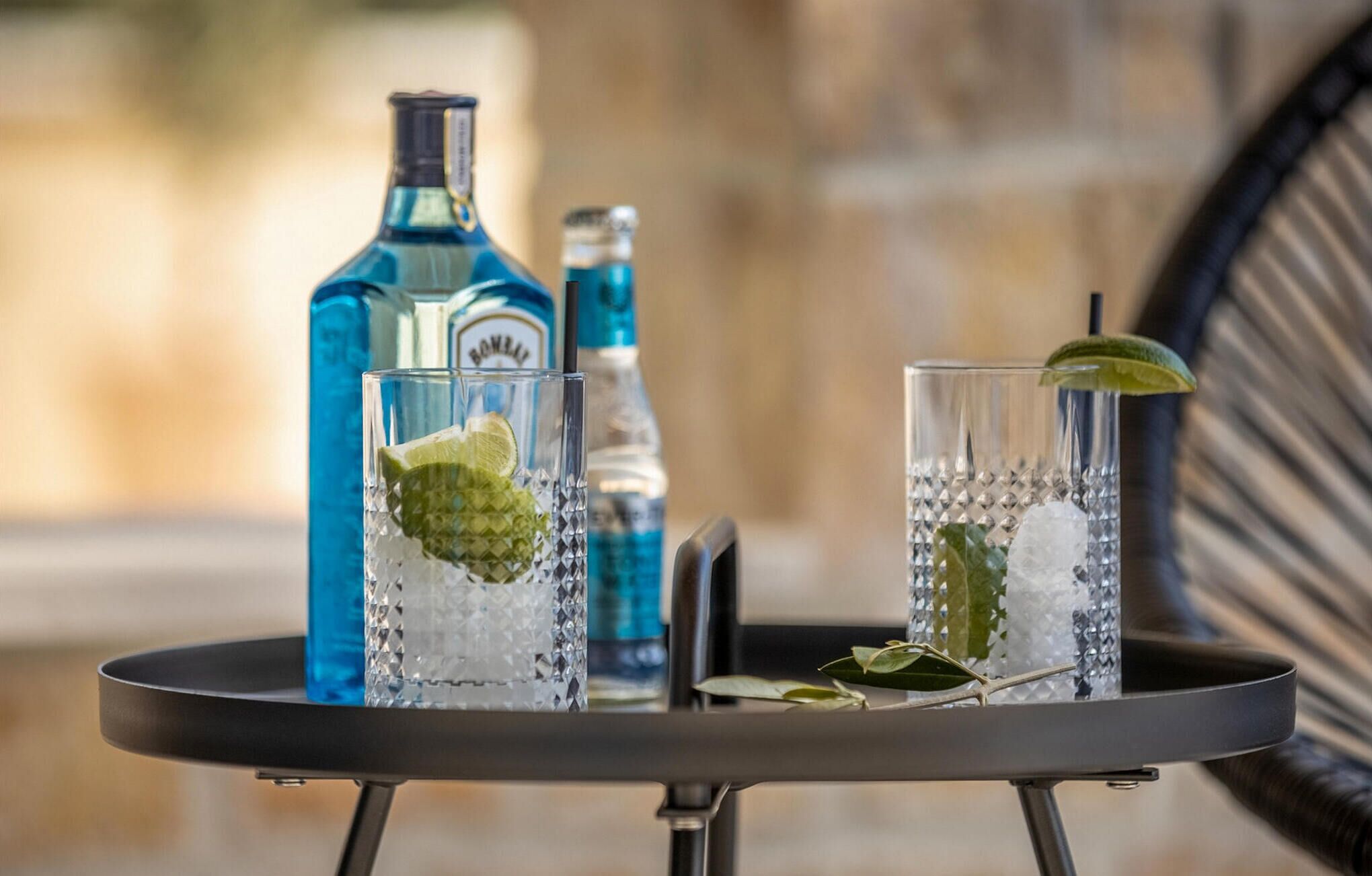 Deux verres contenant une boisson claire, décorés d’une tranche de citron vert et de quelques feuilles de menthe, une bouteille bleue et une bouteille plus petite, le tout posé sur une table.