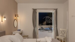 Ein Hotelzimmer mit Bett, Schreibtisch, Stuhl und Blick auf einen Außenpool bei Nacht.