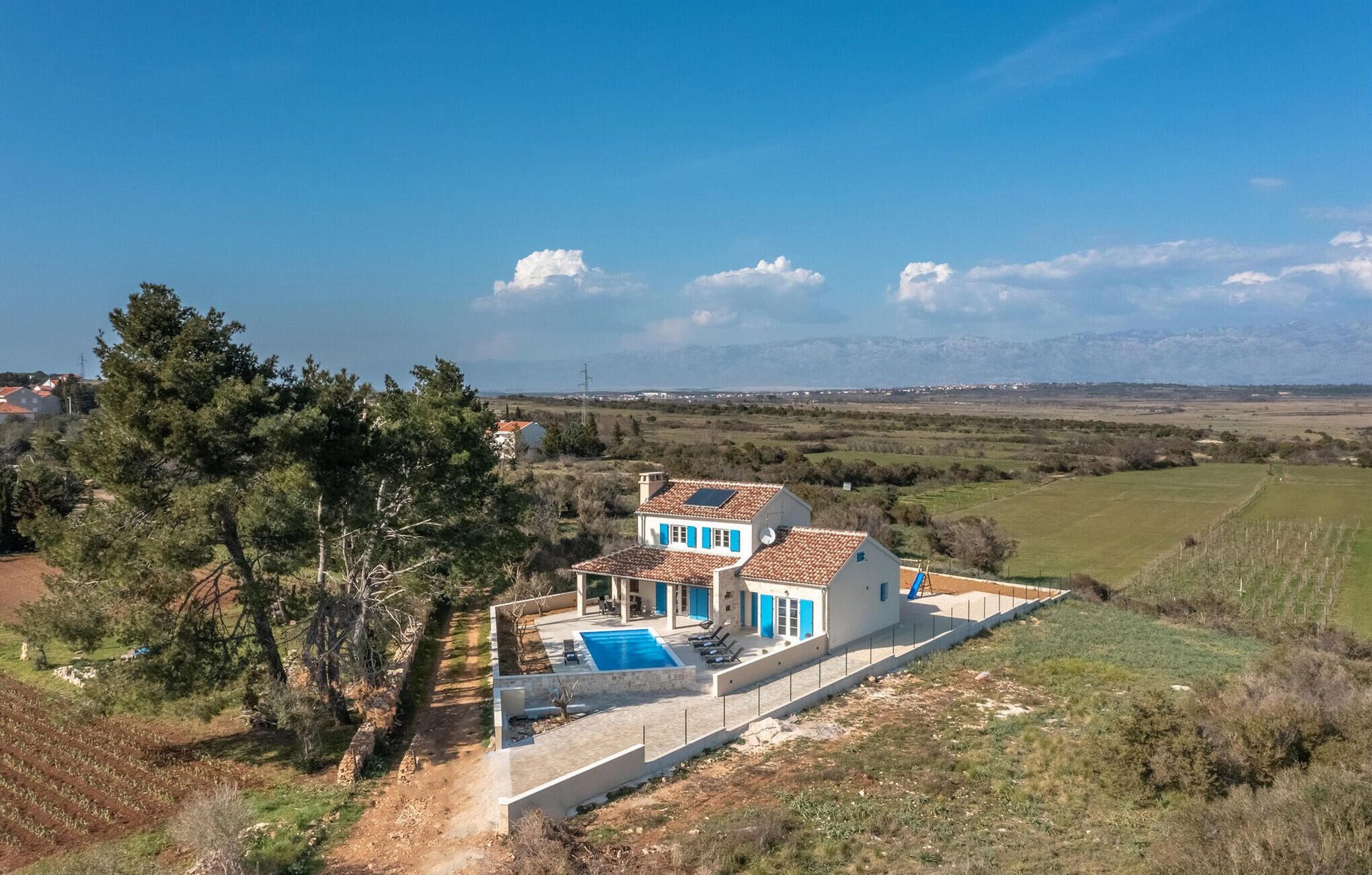 A modern villa with a swimming pool, surrounded by a rural landscape and mountains in the distance.