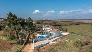 Eine moderne Villa mit Swimmingpool, umgeben von ländlicher Landschaft und Bergen im Hintergrund.