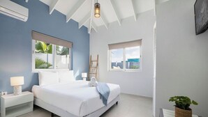 A bedroom with a bed, bedside tables, a lamp, a window with a view, and a ceiling fan. - *NEW* Modern 3BR2BA Home w/ Private Pool & Patio (Oranjestad)