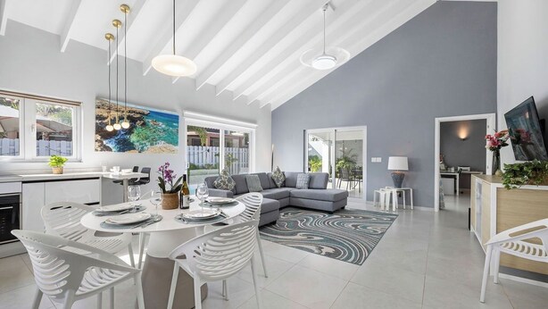 A modern living room with a grey sofa, white chairs, a dining table set, and a large window with a view of the sea. - *NEW* Modern 3BR2BA Home w/ Private Pool & Patio (Oranjestad)