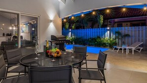 An outdoor patio with a round table set for dining, a grill, and a pool area with lounge chairs. - *NEW* Modern 3BR2BA Home w/ Private Pool & Patio (Oranjestad)