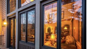 En modern byggnad med stora fönster som speglar träden och en ombonad interiör med en lampa och möbler.