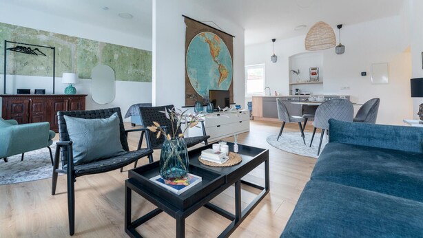 A modern living room with a large world map, a dining area, and a kitchen.