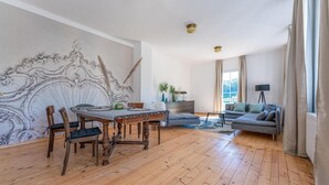 Un salon spacieux doté d’un parquet, d’une table à manger avec des chaises, d’un canapé et d’un grand mur décoratif.