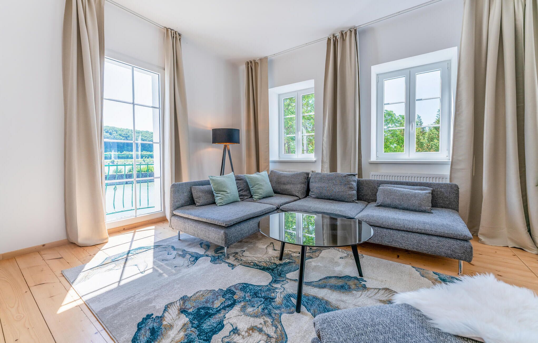 A modern living room with a sectional sofa, large windows, and a view of greenery.