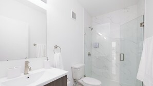A modern bathroom with a white sink, mirror, toilet, and glass shower enclosure. - Serenity Studio - Adorable 1 BR near Florida Keys (Florida City)