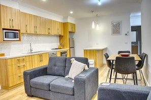 A modern kitchen with wooden cabinets, a microwave, and a dining area with a table and chairs. - Bella - Modern, two bedroom townhouse close to Ballarat CBD (Bakery Hill)