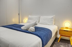 Cozy retreat with a neatly made bed, wooden nightstand, and soft lighting.