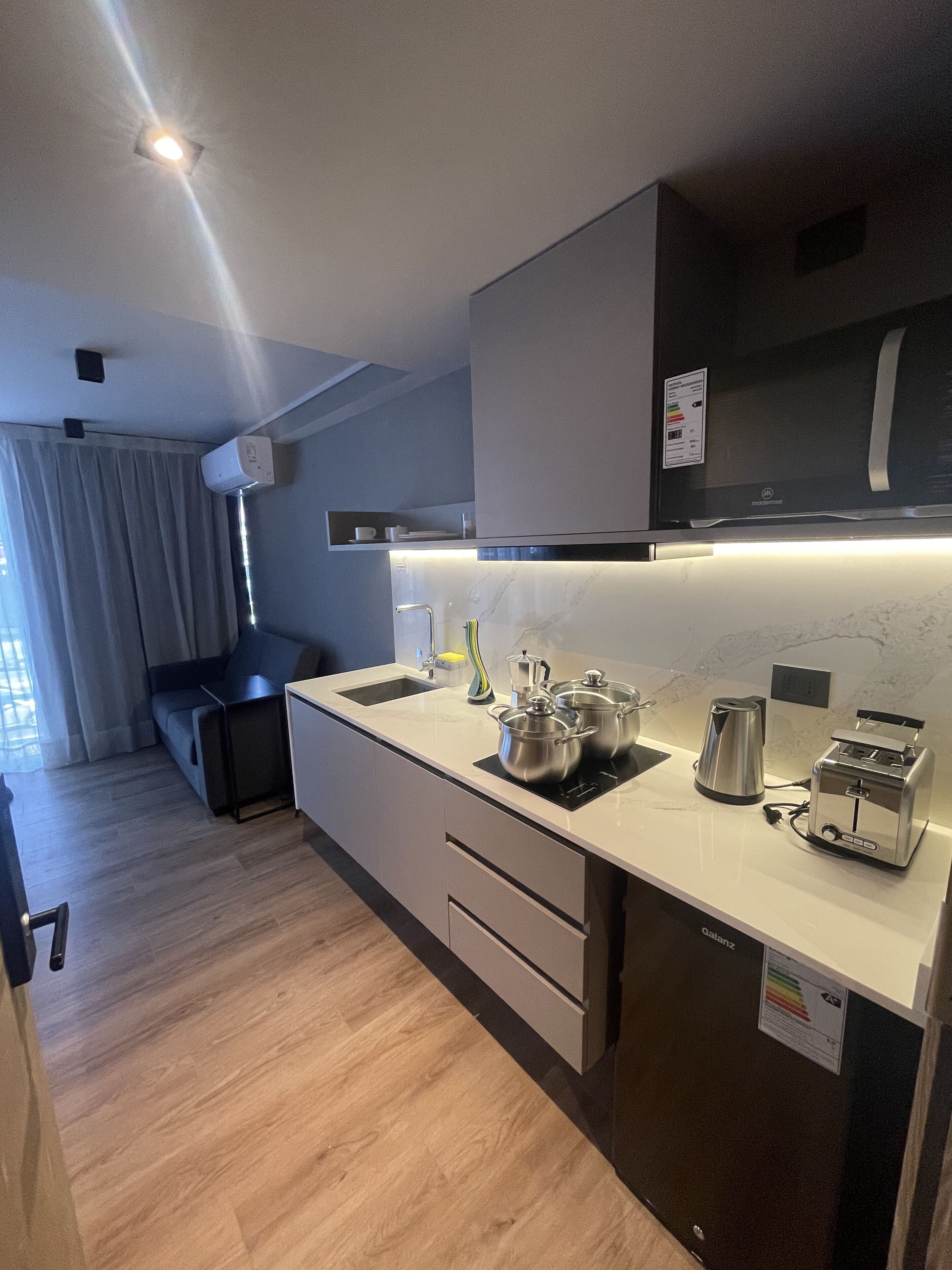 A modern kitchen with a built-in stove, a sink, and a toaster. There is a window with curtains and a ceiling light.