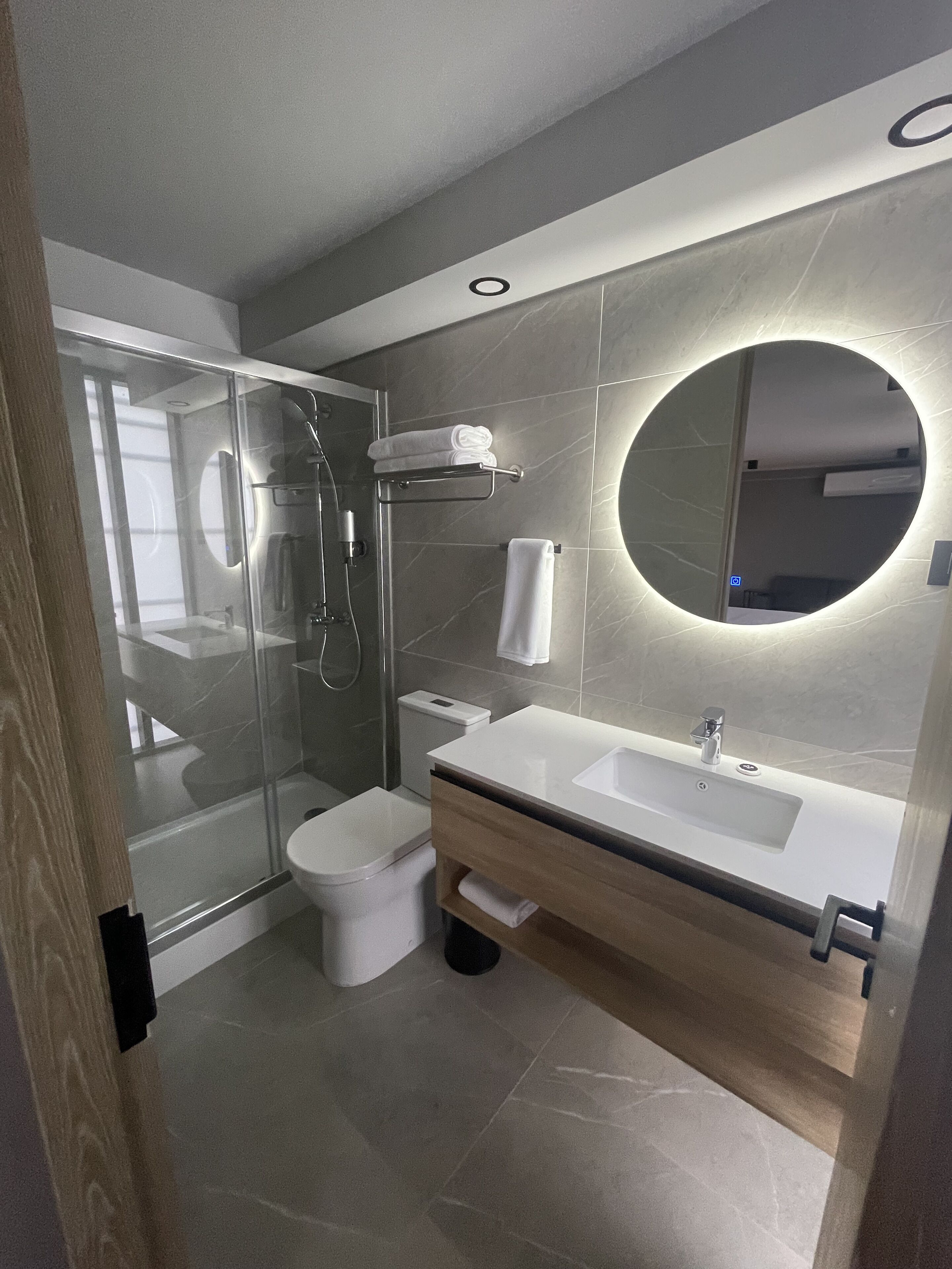 Un baño moderno con ducha envuelta en vidrio, lavamanos blanco y un espejo grande.