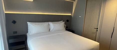 A modern bedroom with a large bed, a bedside table, a wardrobe, and an air conditioning unit.