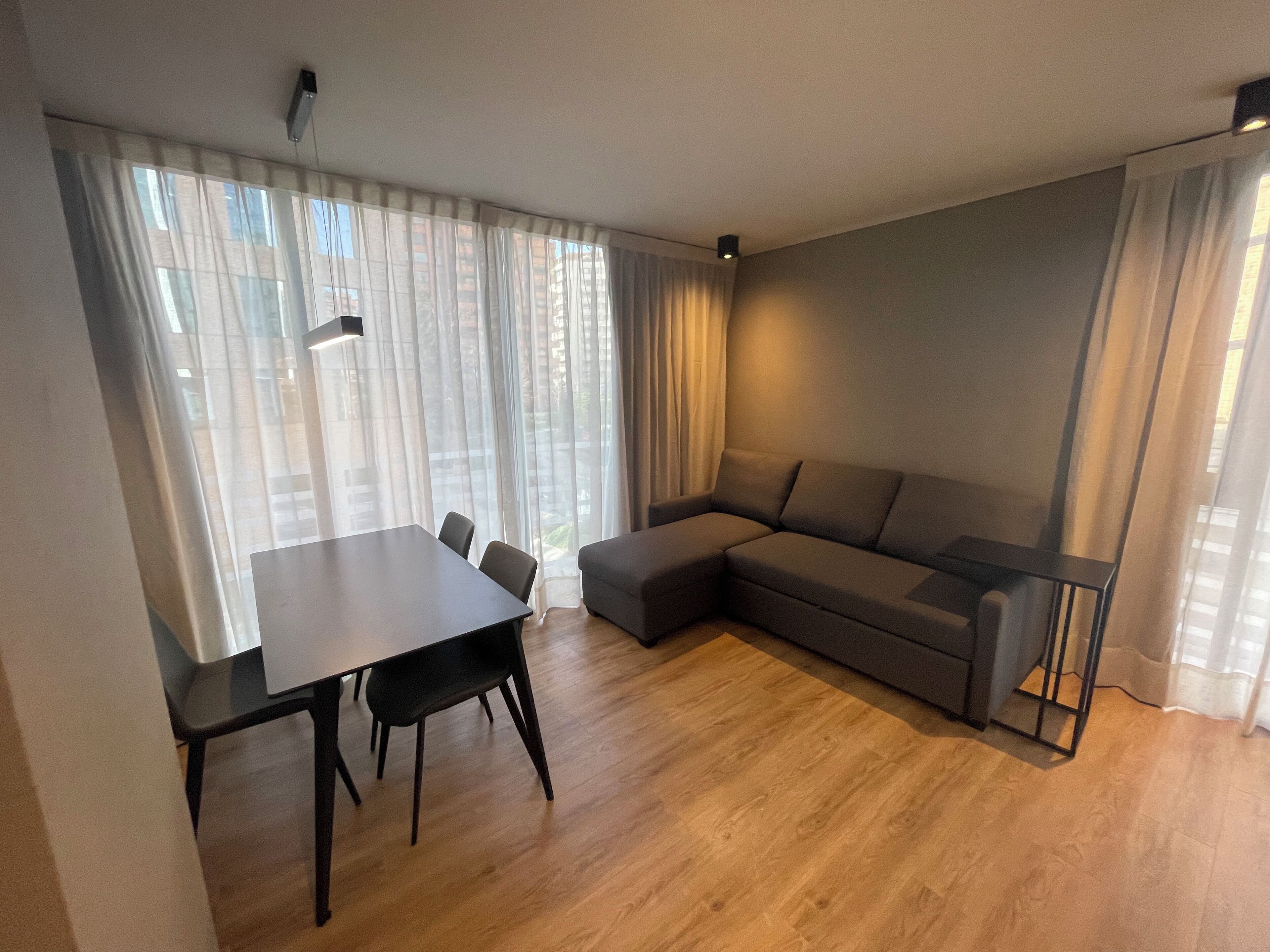 A modern living room with a dining table, a sofa, and sheer curtains.