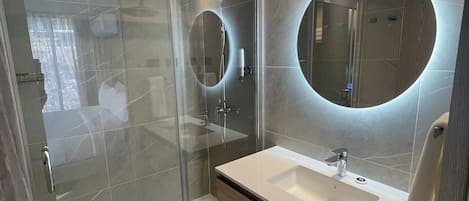 A modern bathroom with a glass-enclosed shower, a round mirror, and a white sink with a wooden vanity.