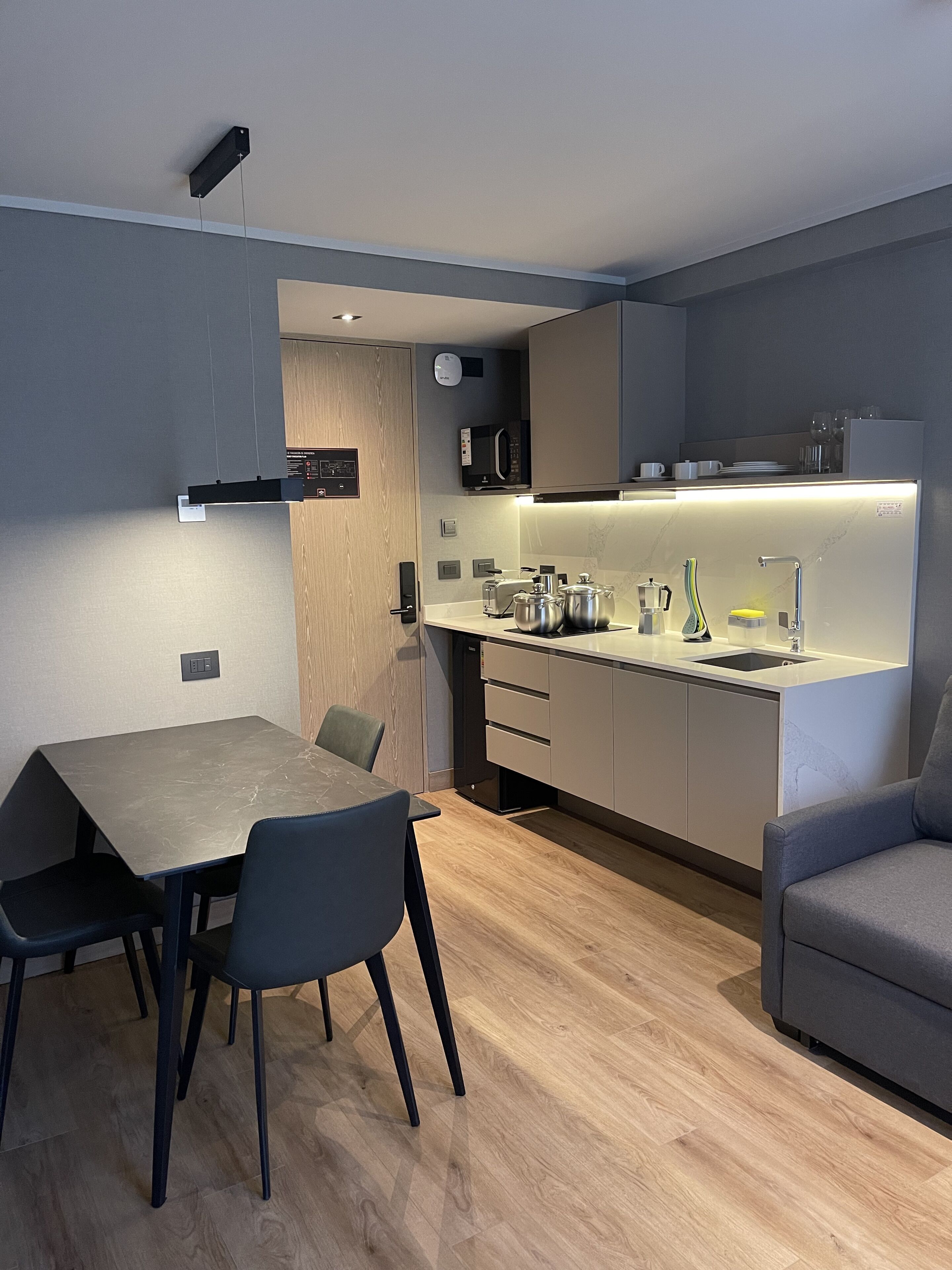 A modern kitchen with a built-in microwave, toaster, and kettle. There is a dining area with a table and chairs.