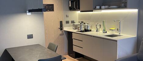 A modern kitchen with a built-in microwave, toaster, and kettle. There is a dining area with a table and chairs.