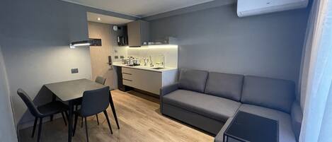 A modern, compact living space with a dining area, kitchenette, and a sofa.
