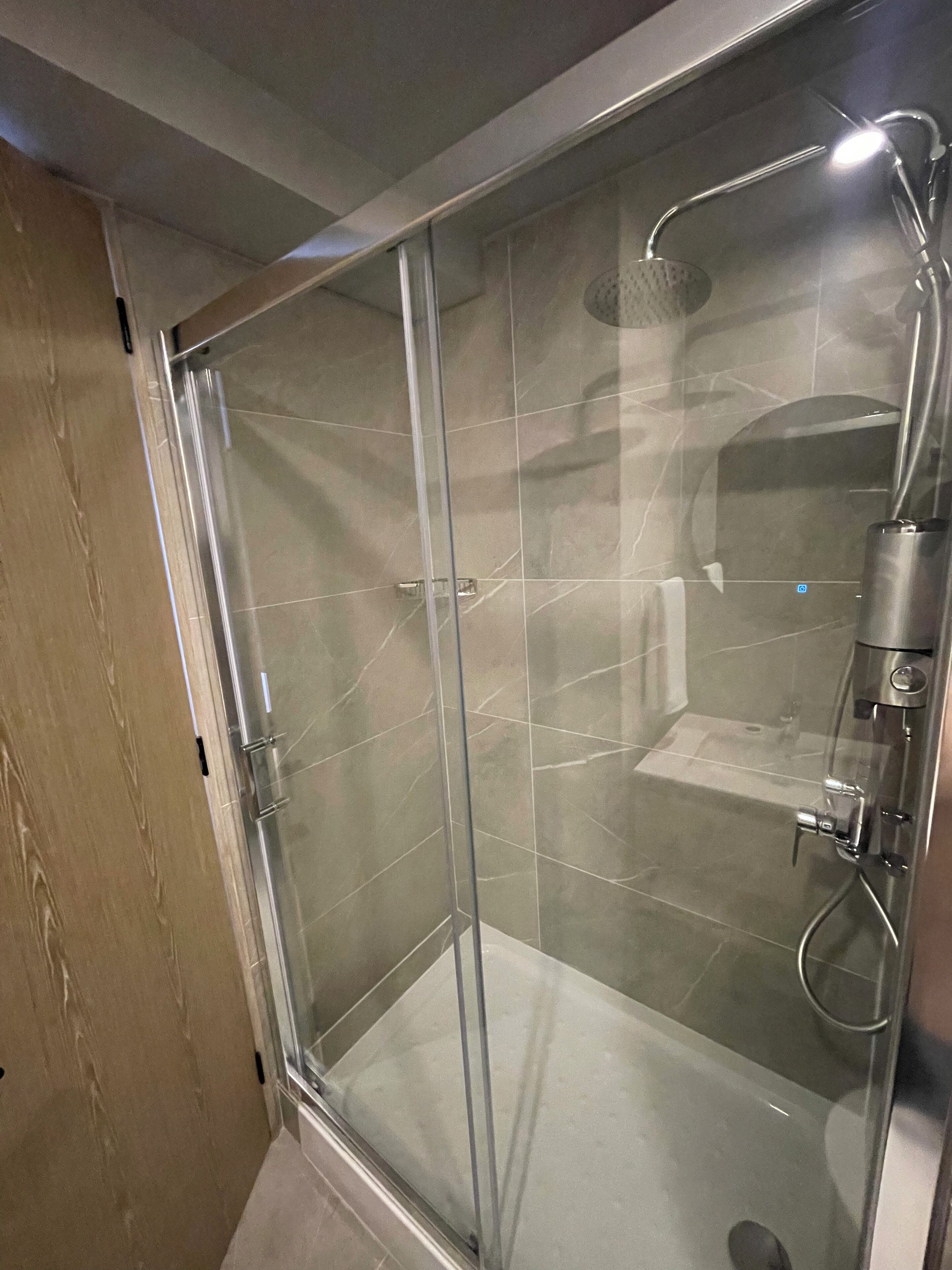 A glass-enclosed shower stall with a handheld showerhead and a handheld mirror.