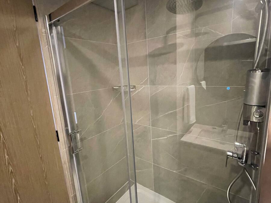 Une cabine de douche fermée par des parois en verre, équipée d’un pommeau de douche à main et d’un miroir à main.