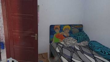 A bedroom with a bed featuring a Naruto-themed headboard, a wooden door, and a small blue water dispenser on the floor.