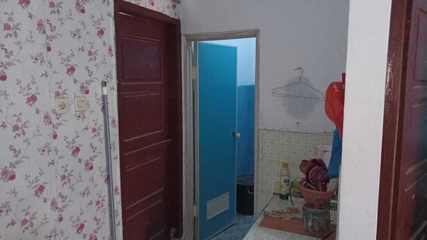 A narrow hallway with a floral-patterned wall, a red door, and a blue door leading to a bathroom.