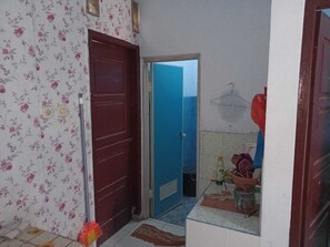 Un couloir étroit avec un mur orné d’un motif floral, une porte rouge et une porte bleue donnant sur une salle de bain.