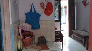 A small kitchen with a tiled backsplash, a blue trash bin, a red bag, and various kitchen items on the counter.